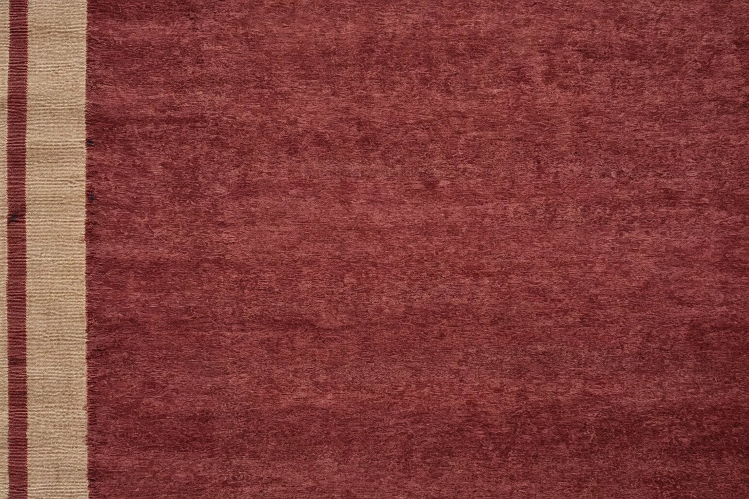 Overhead view of a hand-knotted rug field showing abrash as broad horizontal bands of lighter and deeper red
